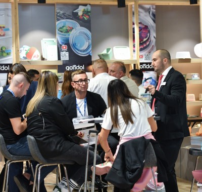  A group of visitors are sitting at the exhibitor's stand, listening attentively to someone's speech.