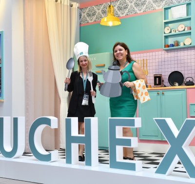 ZUCHEX ekibi, şef şapkaları takarak maket ürünleri sergiledikleri mutfakta poz veriyor ve kameraya neşeyle el sallıyor.